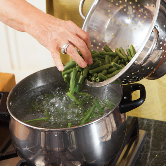 woman putting vegetables into boiling water for blanching